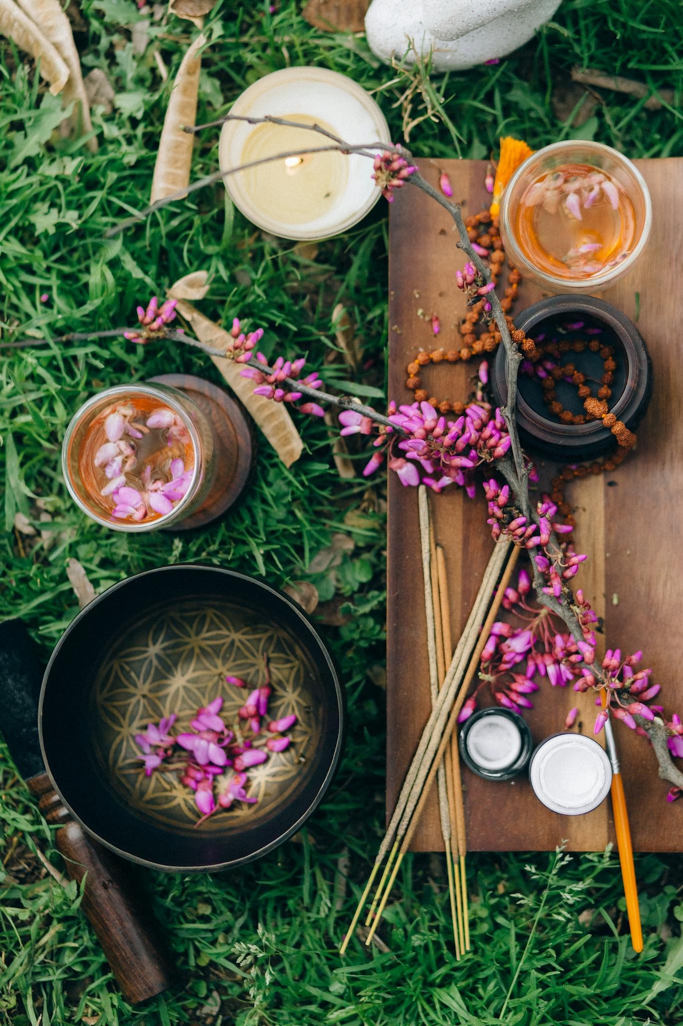 A serene outdoor setup featuring candles, incense, and vibrant pink blossoms on a wooden board.