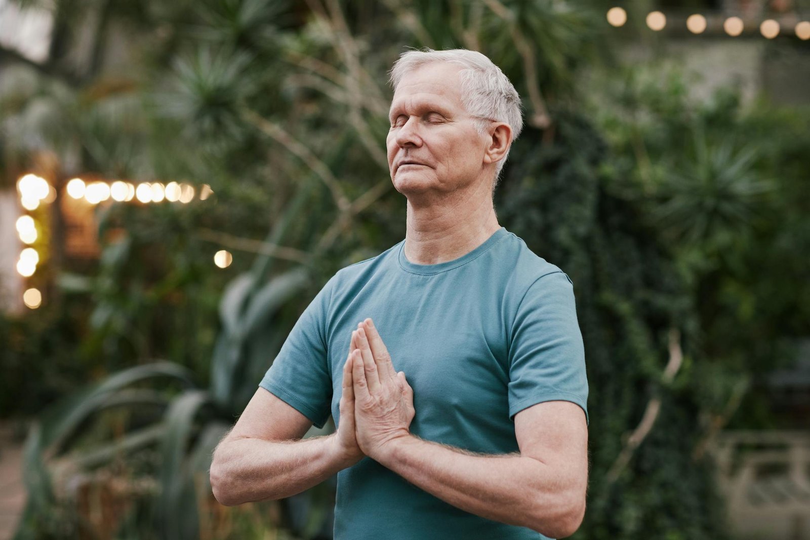 Serene elderly man meditating outdoors in a tranquil garden setting, focusing on peace and mindfulness.