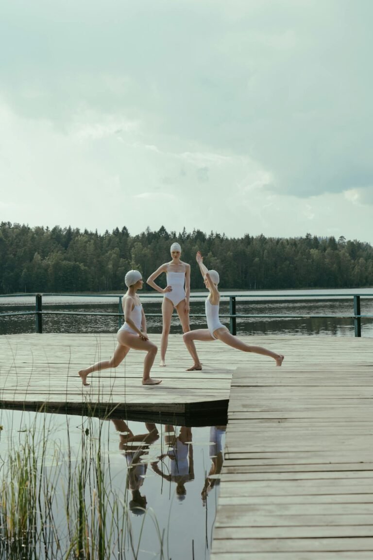 Three women practicing yoga on a peaceful lakeside pier, fostering tranquility with nature.