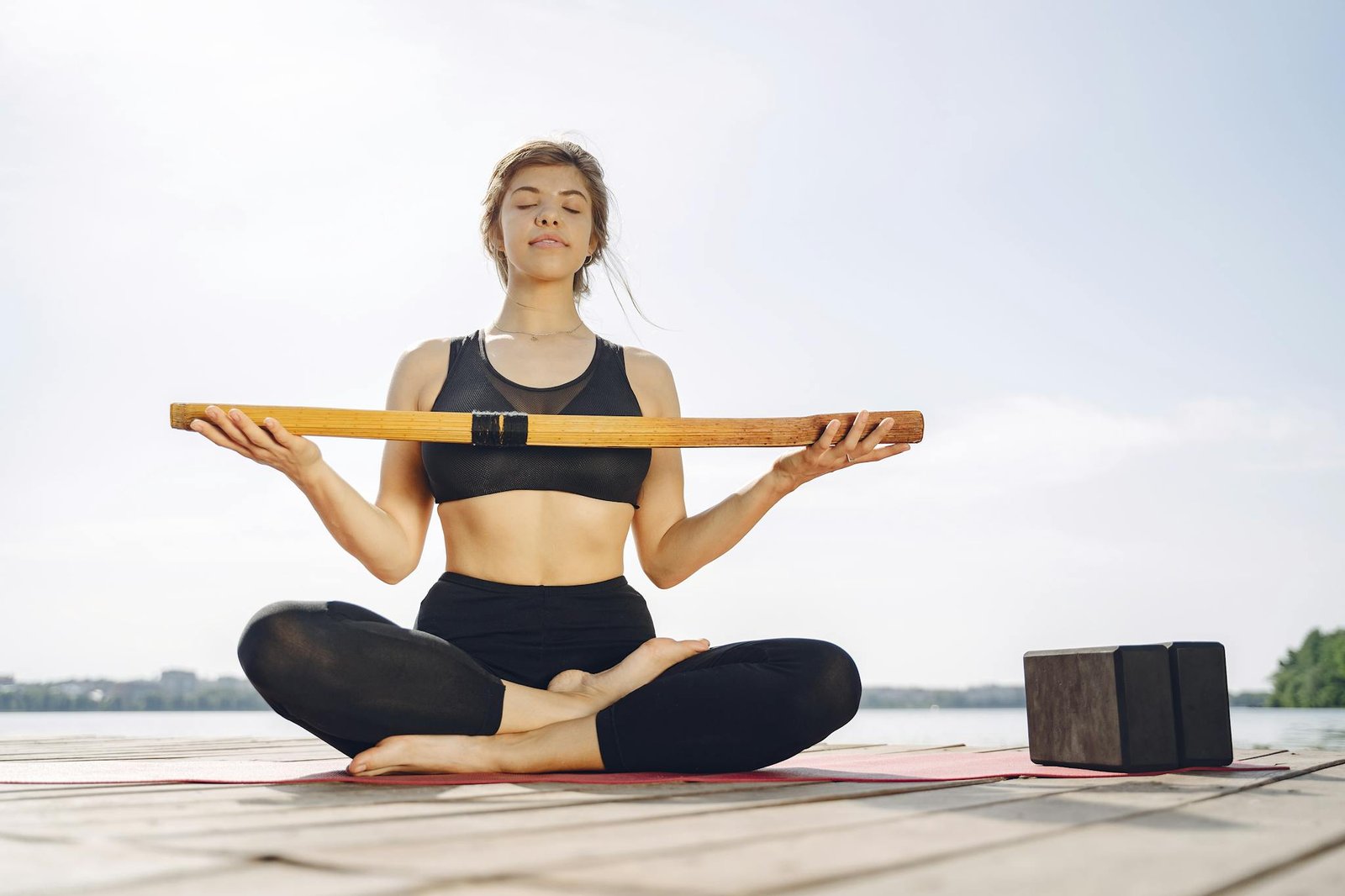 Woman practicing yoga outdoors by a lake with yoga accessories, enjoying a serene environment.